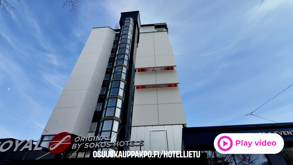 Modern hotel tower with a glass-walled vertical corridor against a clear blue sky, viewed from street level.
